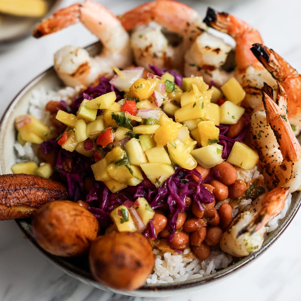 Colorful seafood bowl with grilled shrimp and scallops, mango salsa, purple cabbage, beans, rice, and fried plantains.